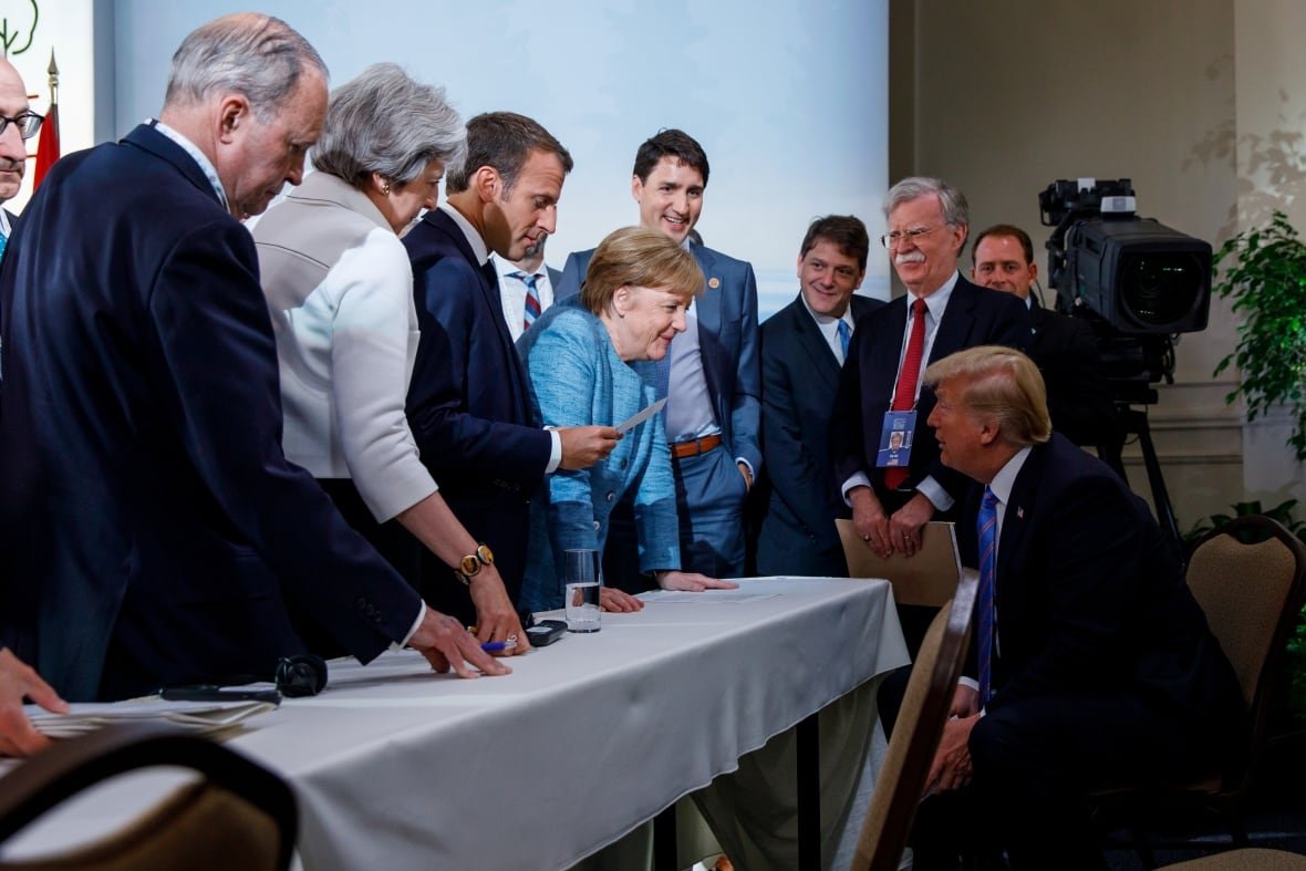 Trump seated at a desk, with other leaders crowded around him