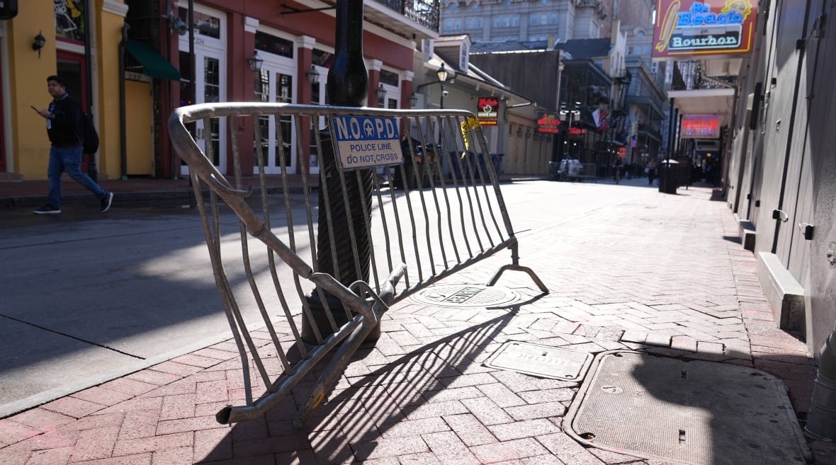 A dented metal barricade leans against a pole on an empty street. It says "Police Line. Do Not Cross" on it.