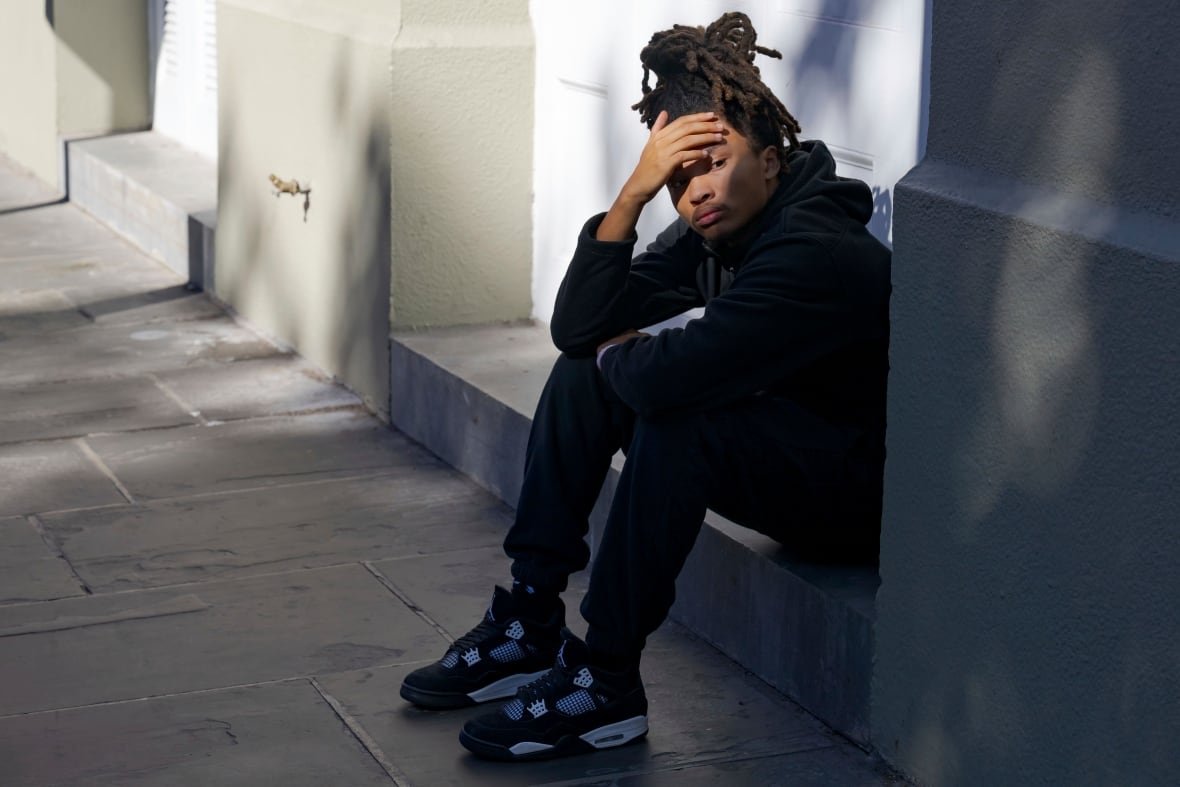 A person sits on a street, shading their eyes.