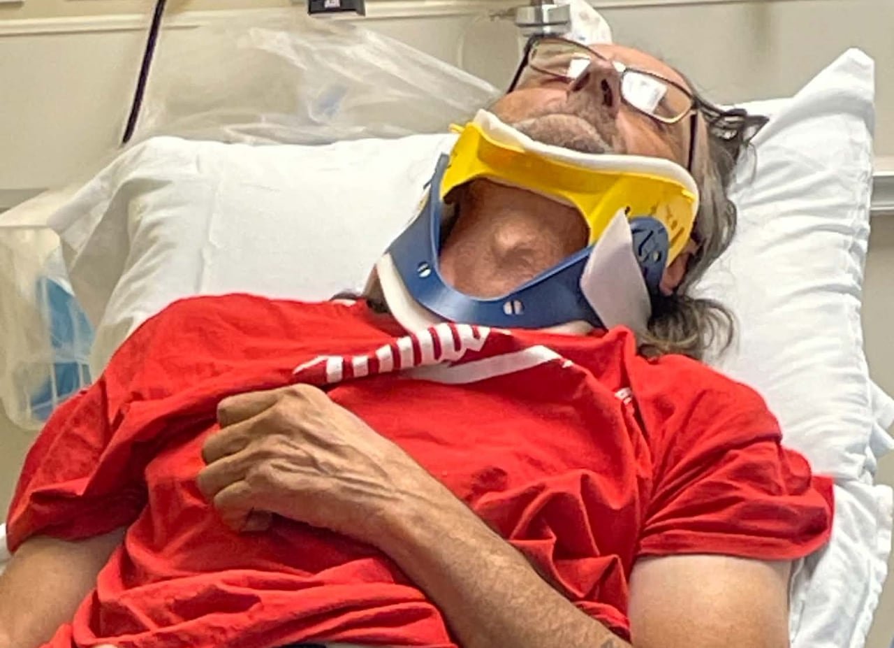 A man lies in a hospital bed with a medical device around his neck.